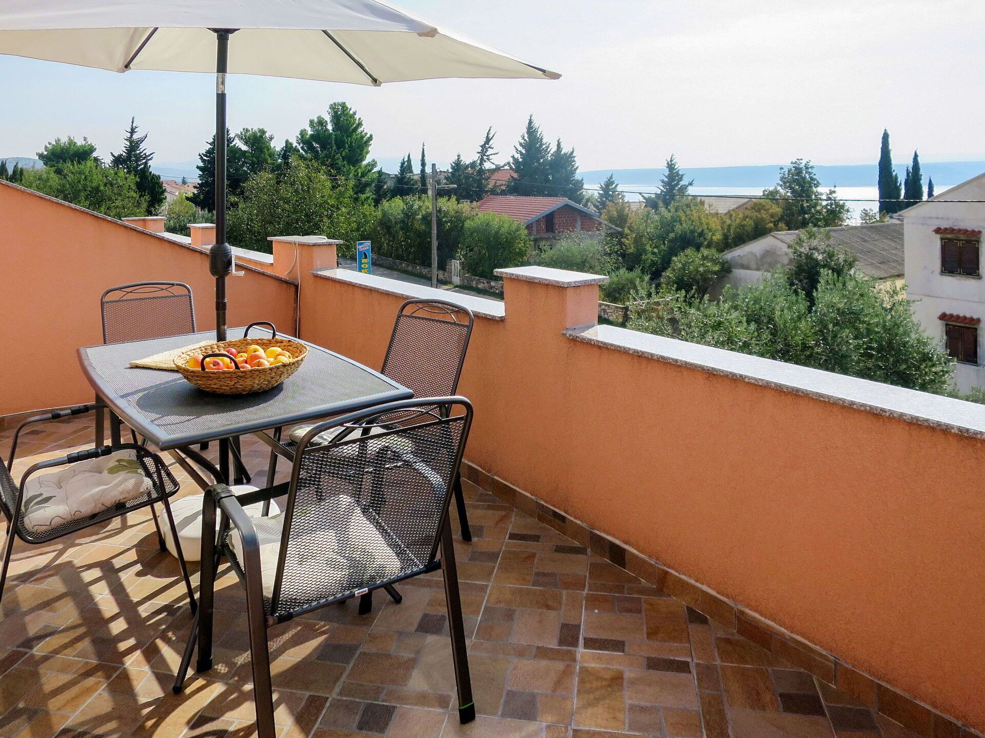 A terrace with a table, chairs, and a basket of fruit.