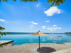 Een strand met een houten bankje, een rieten parasol en rustig blauw water.