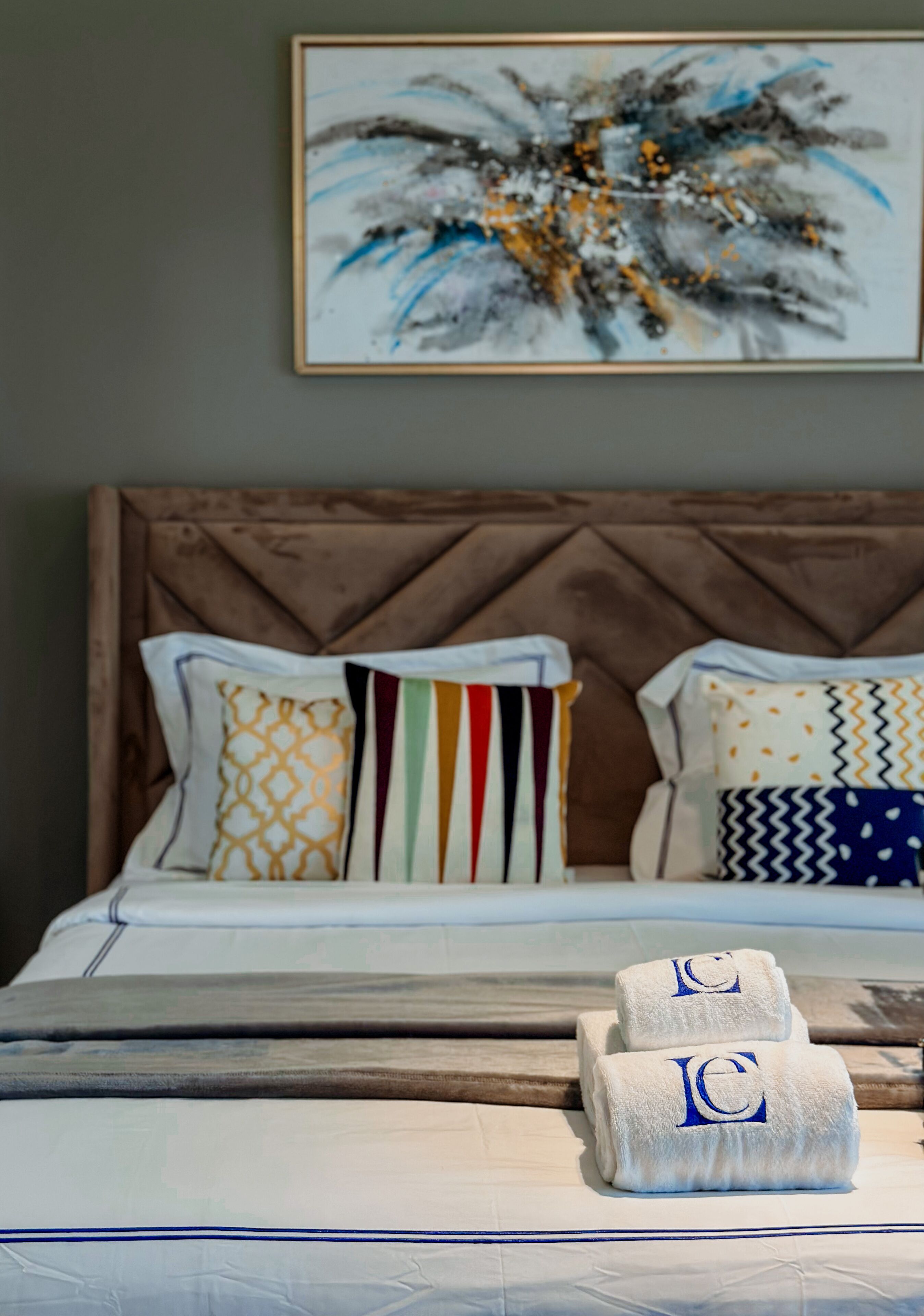 Una cama bien hecha con almohadillas estampadas y un cuadro abstracto enmarcado encima.