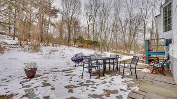 Un patio con una mesa y sillas, rodeado de nieve en el suelo y árboles.