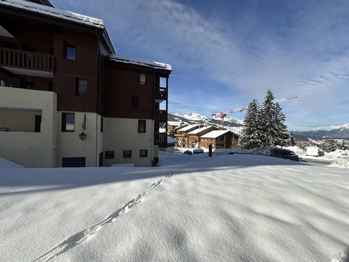 A snow-covered building with a balcony, a snow-covered ground, and a mountain in the background.