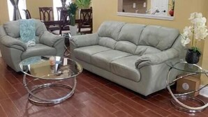 Una sala de estar con un sofá gris, una mesa de centro de vidrio y un comedor con una araña.