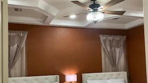 Habitación de hotel con dos camas, un ventilador de techo y una mesita de noche con lámpara.