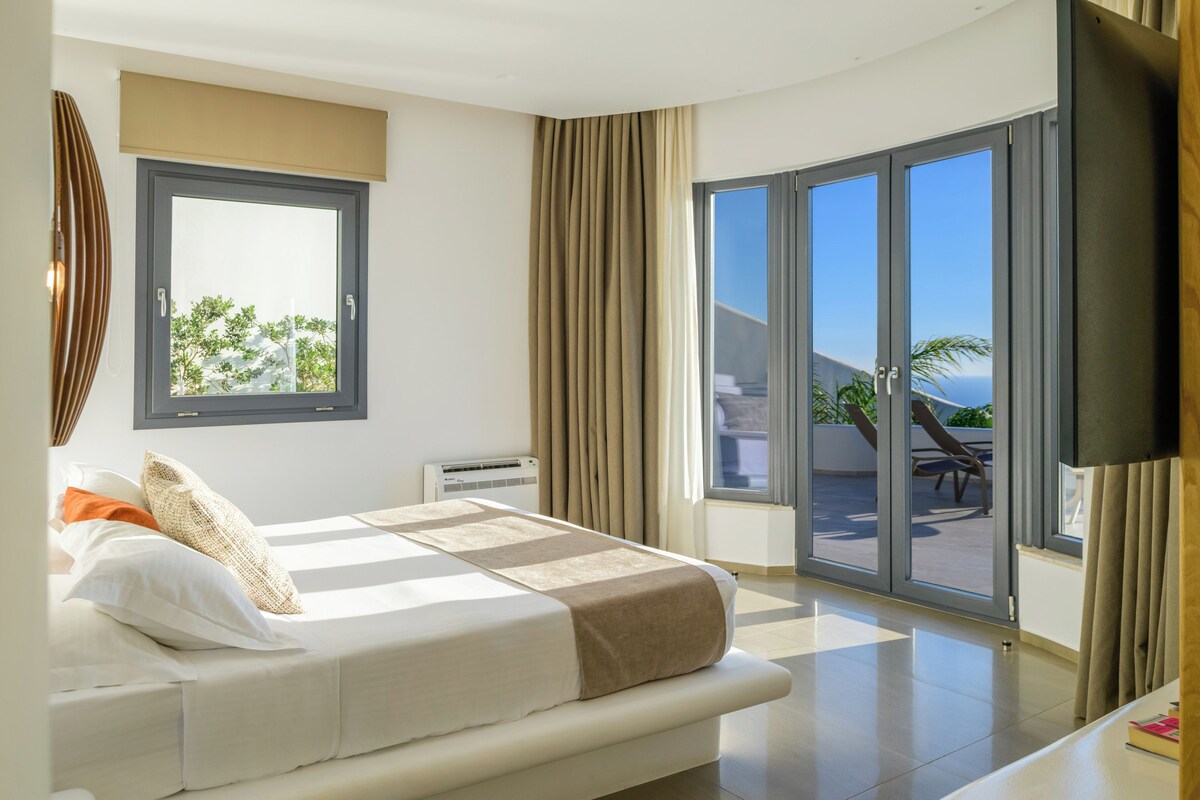 A modern bedroom with a bed, a TV, and a balcony with a view.