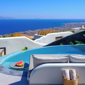 A poolside area with a view of the sea, a lounge chair, and a basket with towels. - Secret Path Luxury Villas (Santorini)