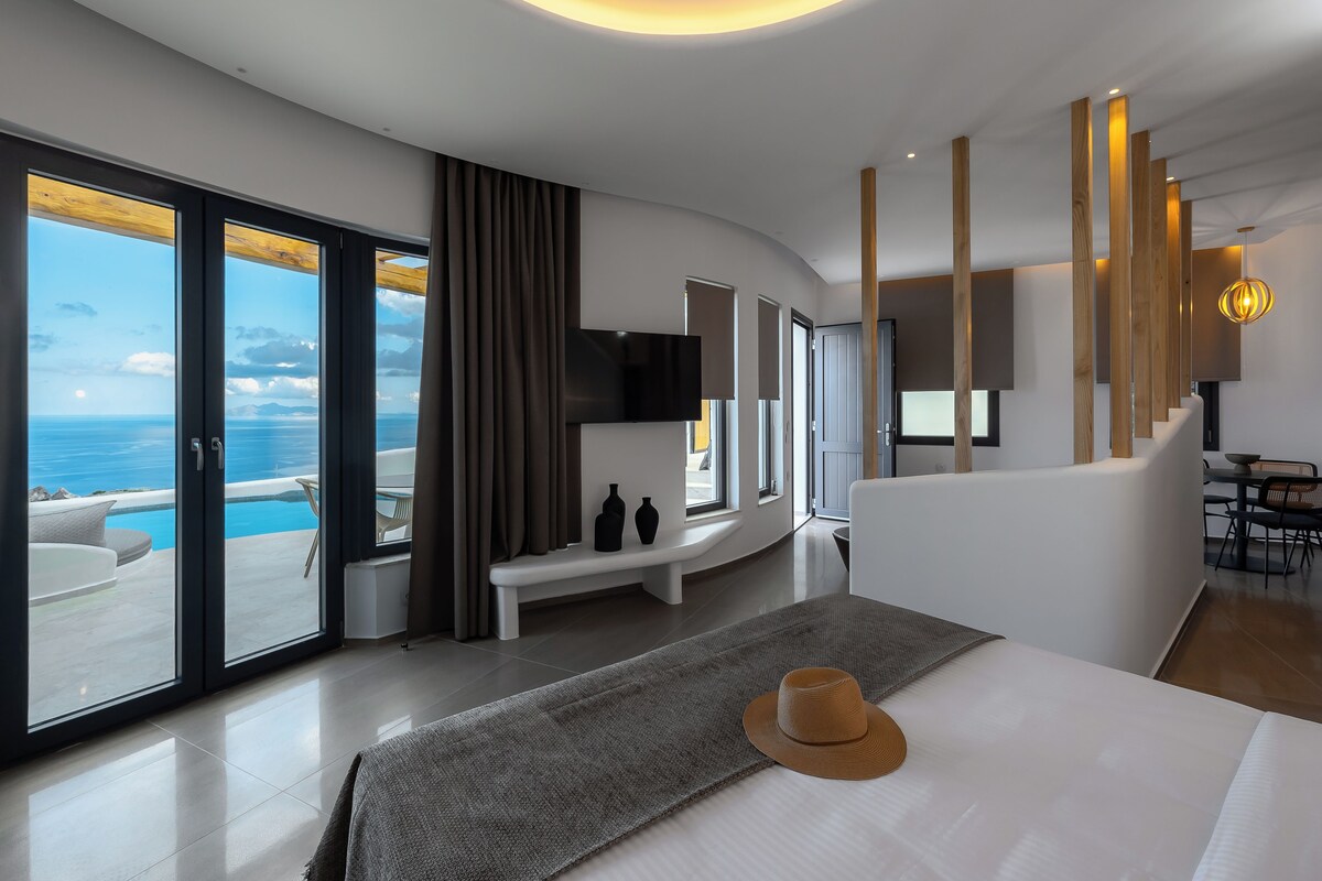 Una habitación de hotel moderna con una cama grande, vistas al mar, un balcón y un comedor.