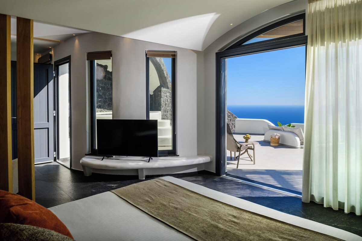 A modern hotel room with a large window, a flat-screen TV, and a view of the ocean.