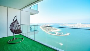 Un balcon agrémenté d’un fauteuil suspendu, d’une rambarde en verre et offrant une vue sur le paysage urbain de la côte.