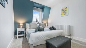 Une chambre à coucher comprenant un lit, des tables de chevet, une fenêtre, un radiateur et un tableau accroché au mur.