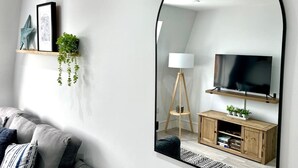 Un salon moderne avec un grand miroir, un téléviseur à écran plat, un meuble TV en bois, une lampe sur pied et un canapé.