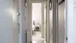 Un couloir qui mène à une chambre à coucher, où se trouvent un lit, une table de chevet et une lampe.