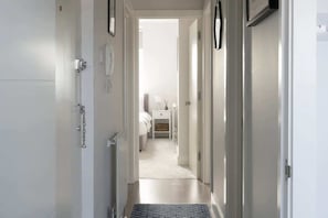 A hallway leading to a bedroom with a bed, bedside table, and a lamp. - Spacious Condo w/ City View & Free Parking (Portsmouth)