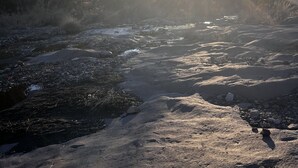Un río con luz solar reflejada en el agua, rodeado de terreno rocoso y vegetación escasa.
