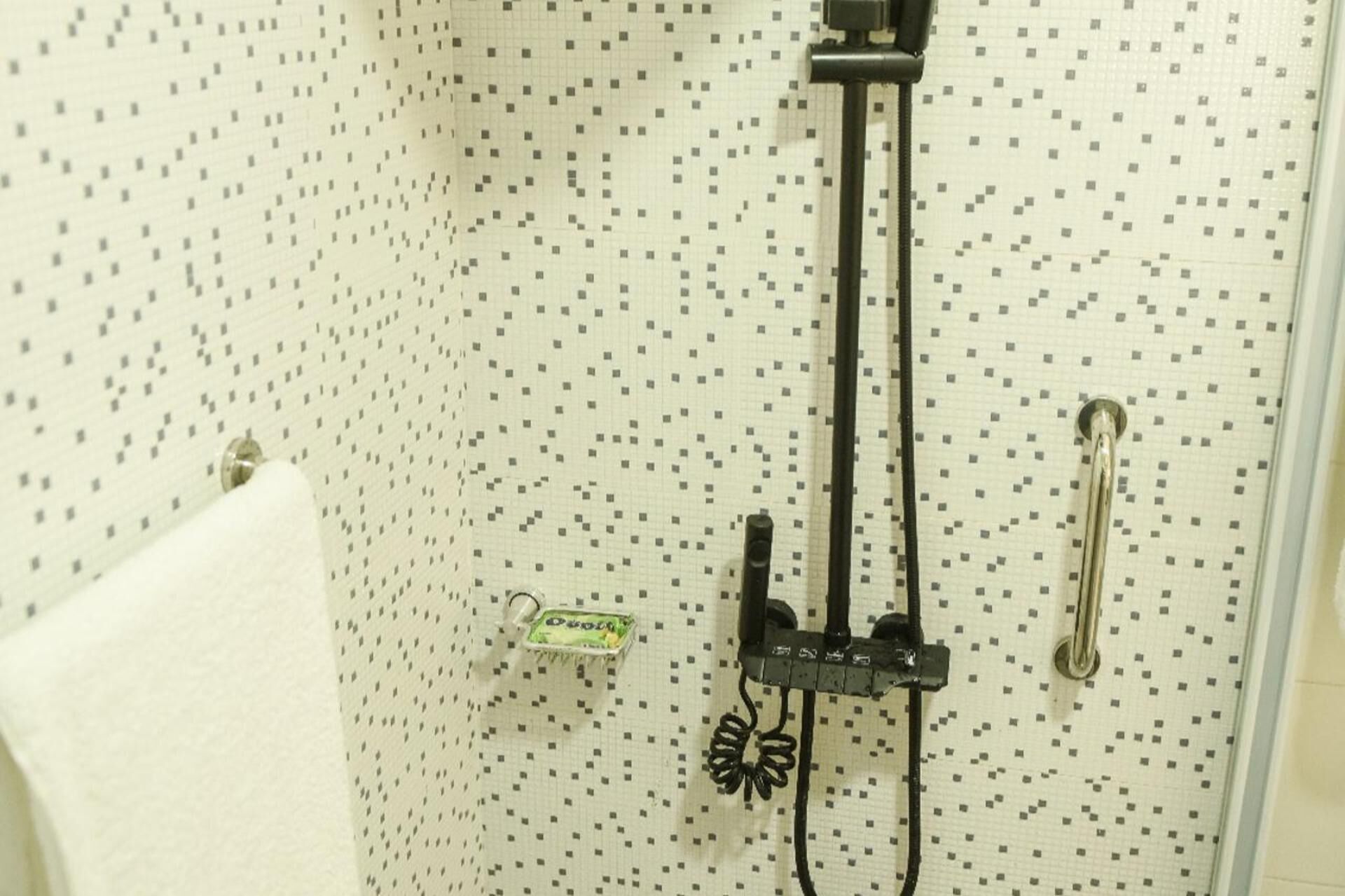 Un baño con pared de azulejos, toallero y cabezal de ducha.