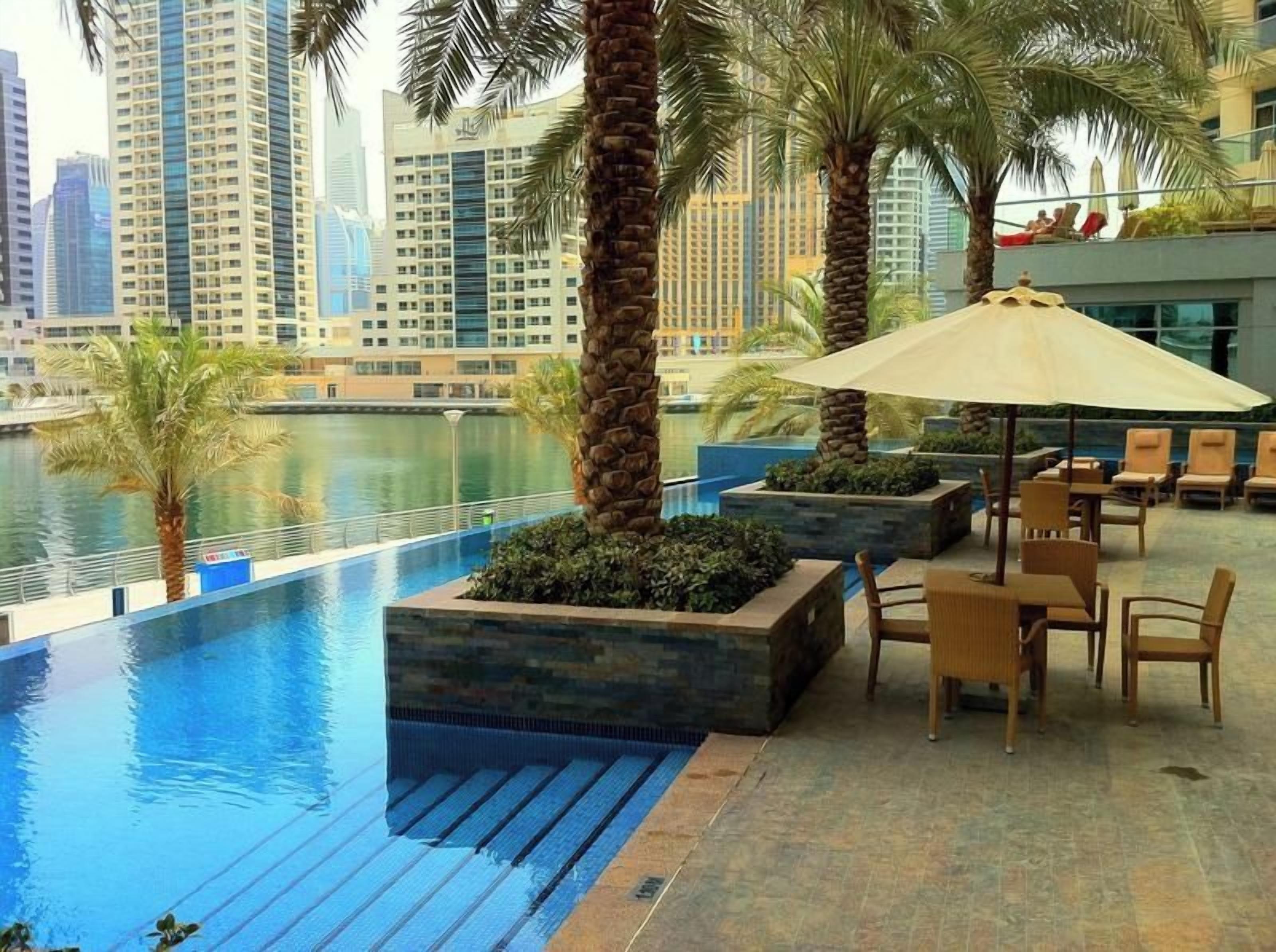 A rooftop pool area with lounge chairs and umbrellas, overlooking a cityscape.