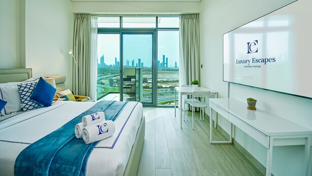 Una habitación de hotel moderna con una cama grande, un escritorio y vistas a la ciudad a través de ventanales de gran altura.