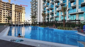 A swimming pool with a person in the water, surrounded by modern buildings, some under construction.