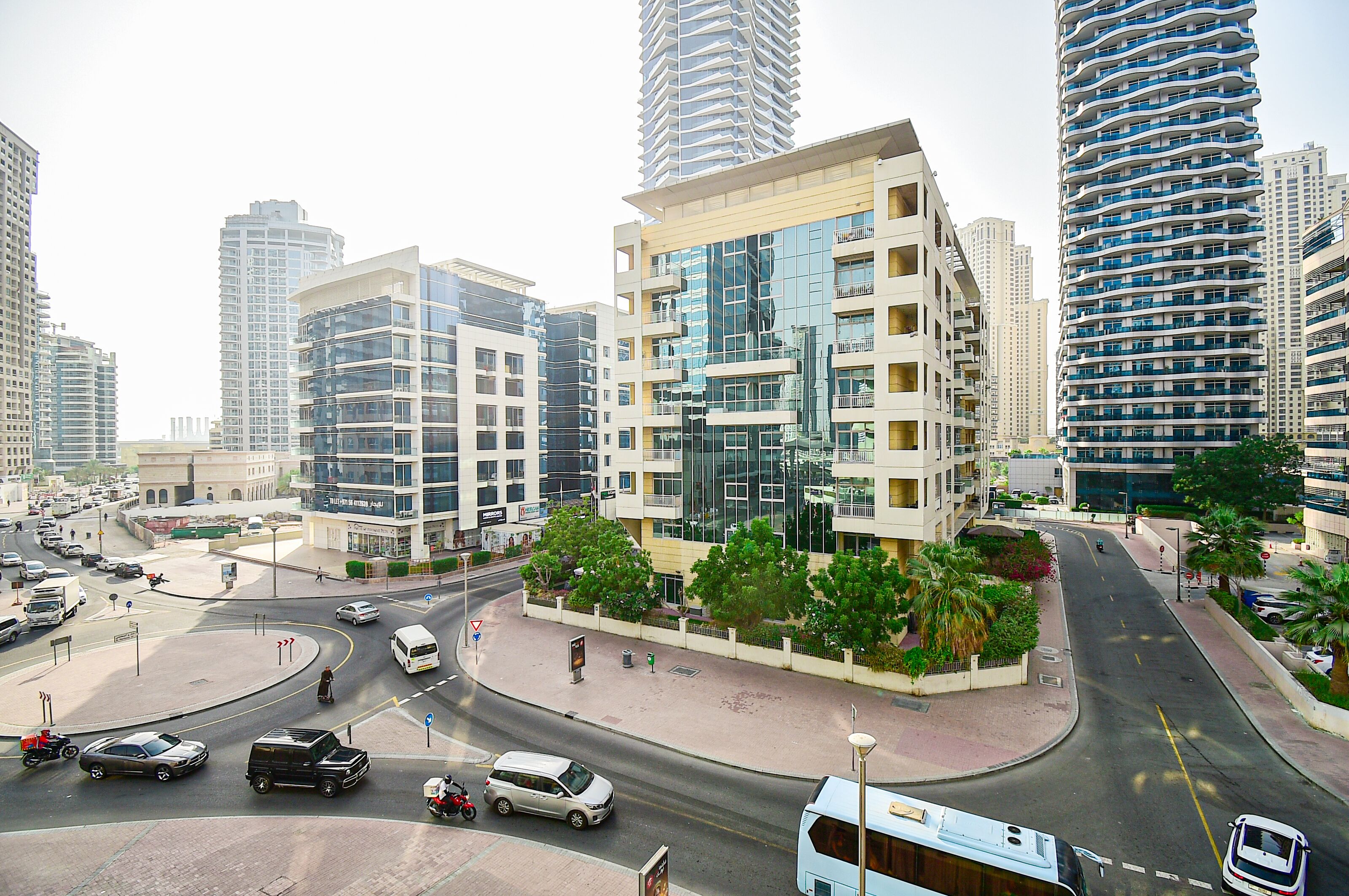 A modern urban intersection with high-rise buildings, a roundabout, and a pedestrian walkway.