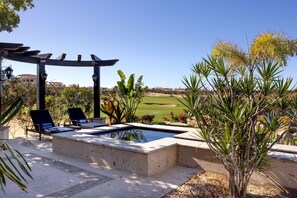 Ein Poolbereich mit Liegestühlen, einer Pergola und Blick auf einen Golfplatz.