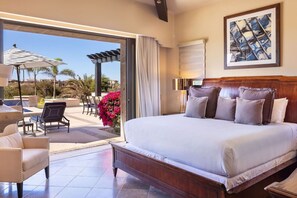 Ein Schlafzimmer mit einem großen Bett, einem Sessel, einem Tisch und Blick ins Freie.