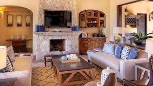 A living room with a stone fireplace, a television mounted above it, and a sofa with decorative pillows. - 5-BR Luxury Golf Villa Retreat (Cabo San Lucas)