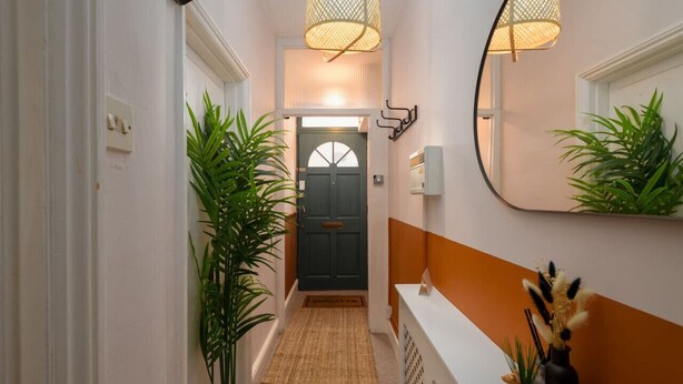 A hallway with a door, a mirror, and a plant.