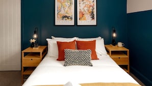 A bedroom with a bed, two nightstands, two wall-mounted lamps, and two framed artworks.