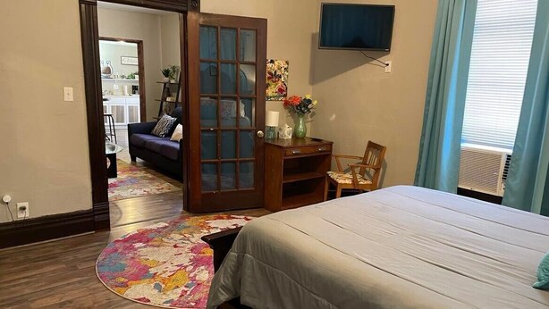 Un dormitorio con una cama, un escritorio, una silla, un televisor y una puerta que da a otra habitación.