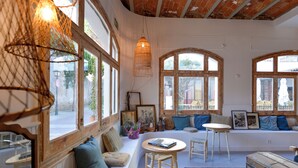 Una habitación acogedora con un banco de madera, una mesa redonda y un ventanal de varios paneles.