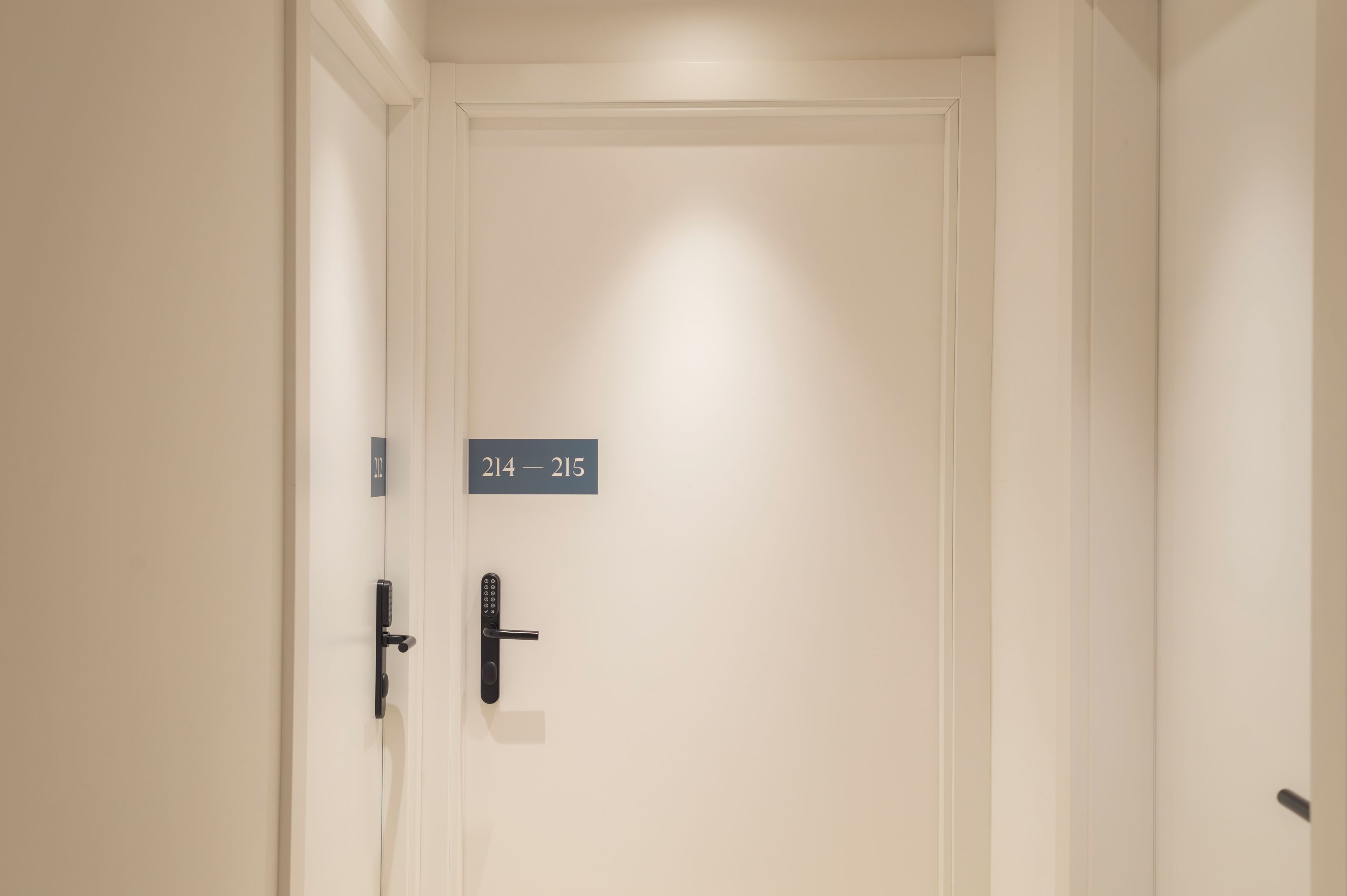 A white door with a digital lock and a sign above it indicating room numbers 214-215.