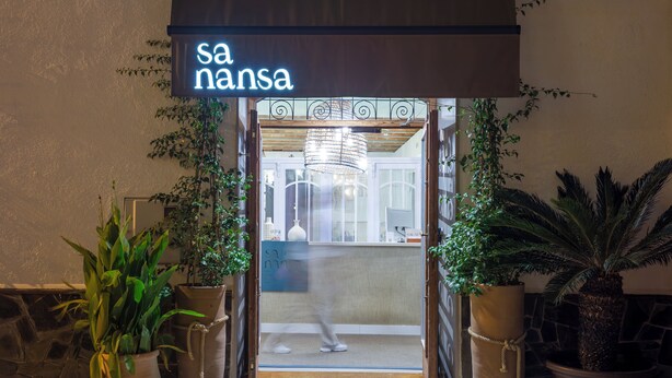 Entrada de hotel con letrero de neón, plantas en macetas y el interior a la vista a través de la puerta.