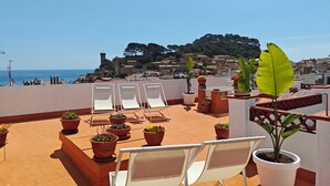 Terraza en la azotea con sillones blancos, plantas en macetas y vistas al mar y edificios históricos.