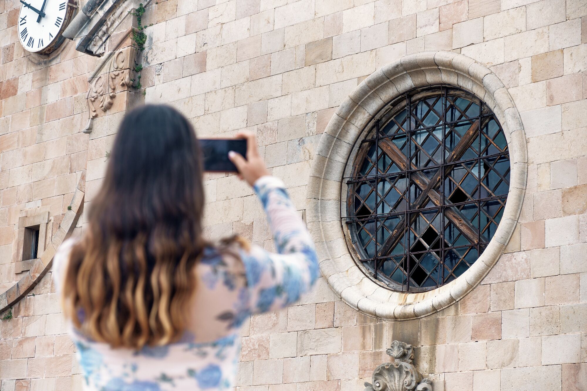 Eine Person fotografiert ein Gebäude mit einem großen, verzierten Fenster und einer Wanduhr.