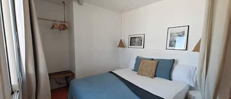 Un dormitorio con una cama, una lámpara colgante, un banco y un perchero de pared.