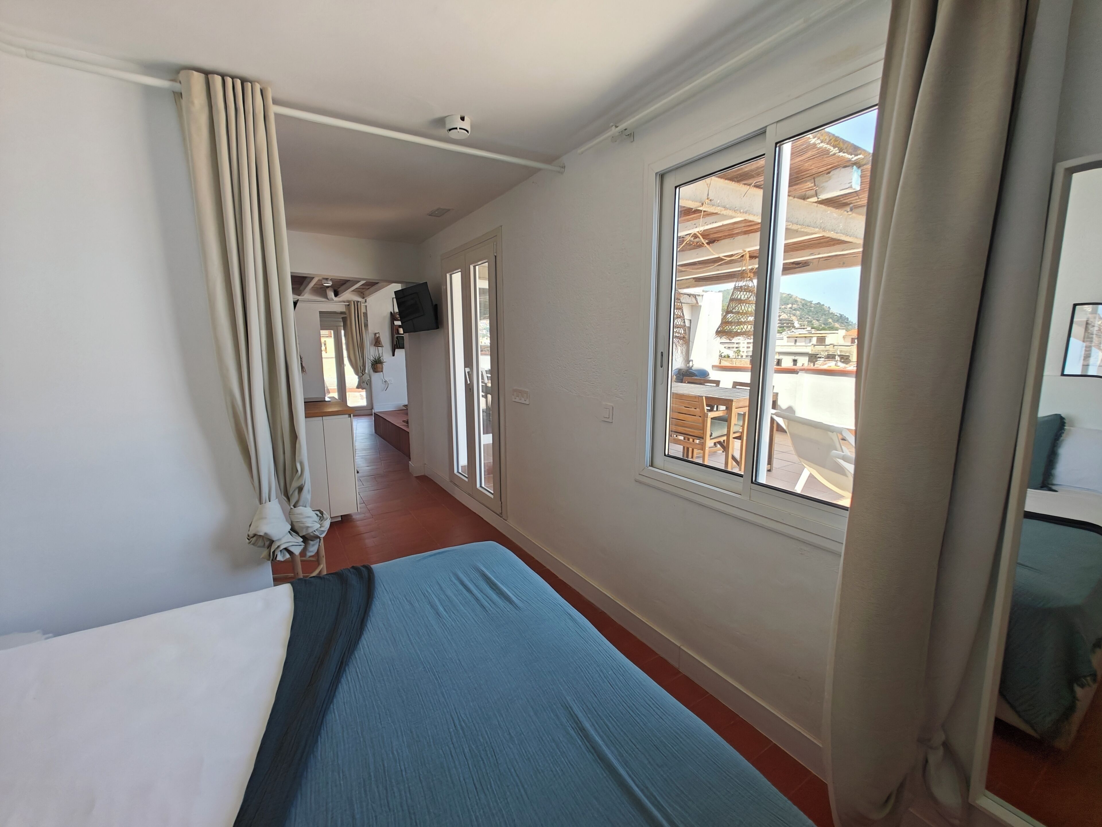 A hotel room with a bed, a window with a view of the outside, a door leading to another room, and a ceiling-mounted light fixture.