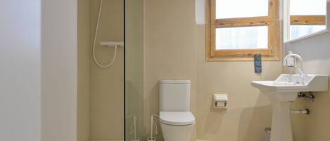 A bathroom with a glass shower enclosure, a toilet, and a sink.