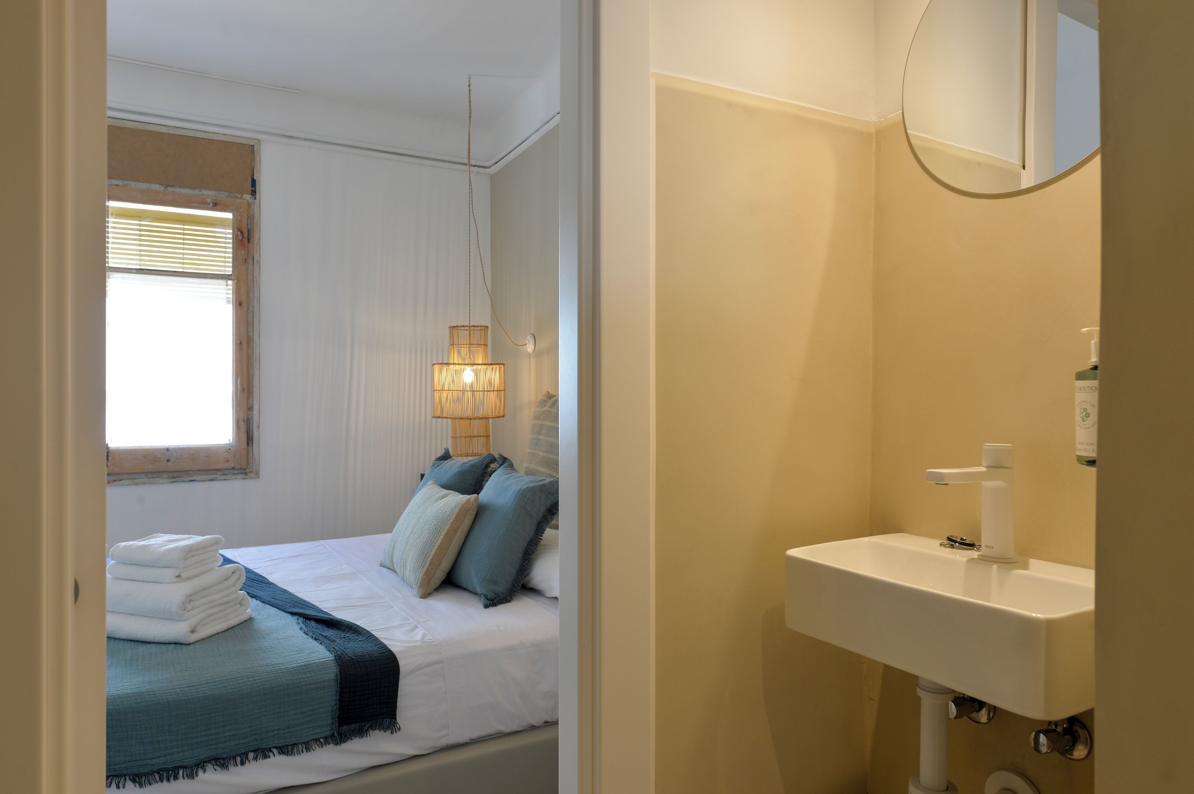 Une chambre à coucher comprenant un lit, une lampe de chevet, une fenêtre et une salle de bain avec un lavabo et un miroir.
