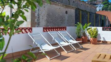 Eine Terrasse mit weißen Liegestühlen, Topfpflanzen und einem gefliesten Boden.