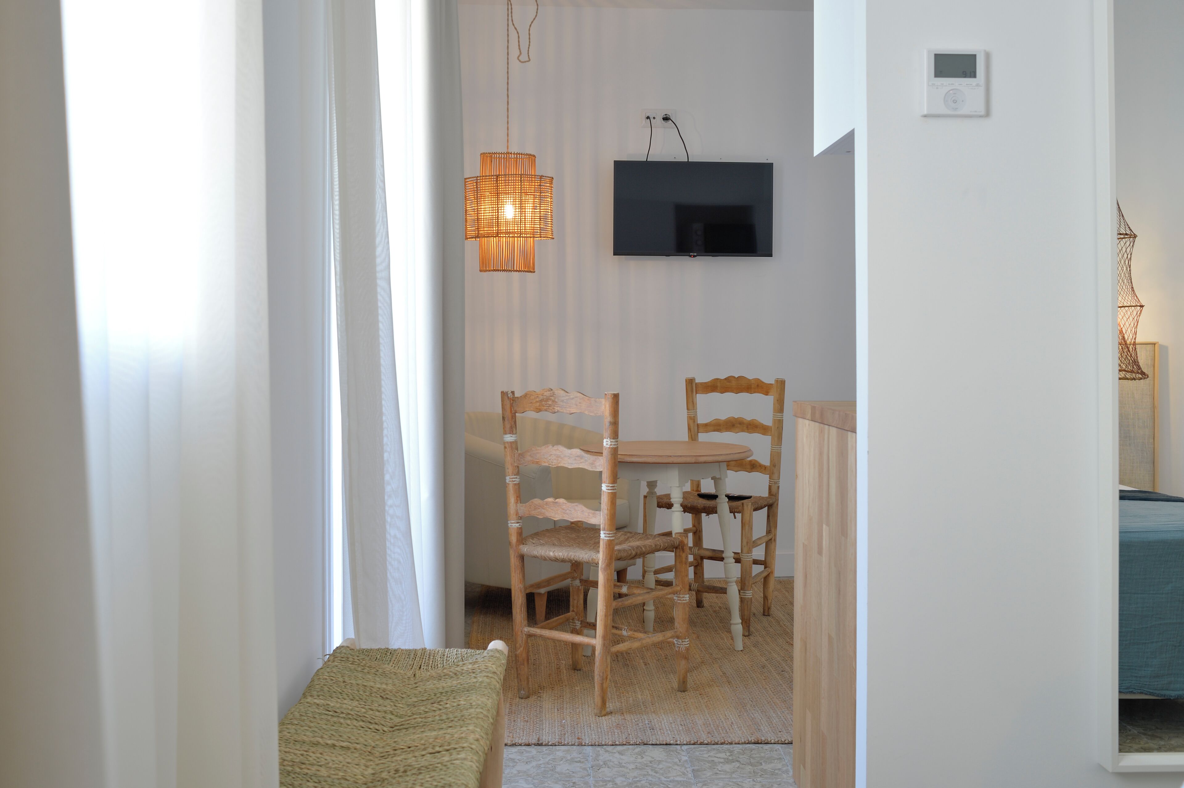 Una habitación con una mesa de comedor y sillas, un televisor fijado a la pared y una lámpara de pie de mimbre.