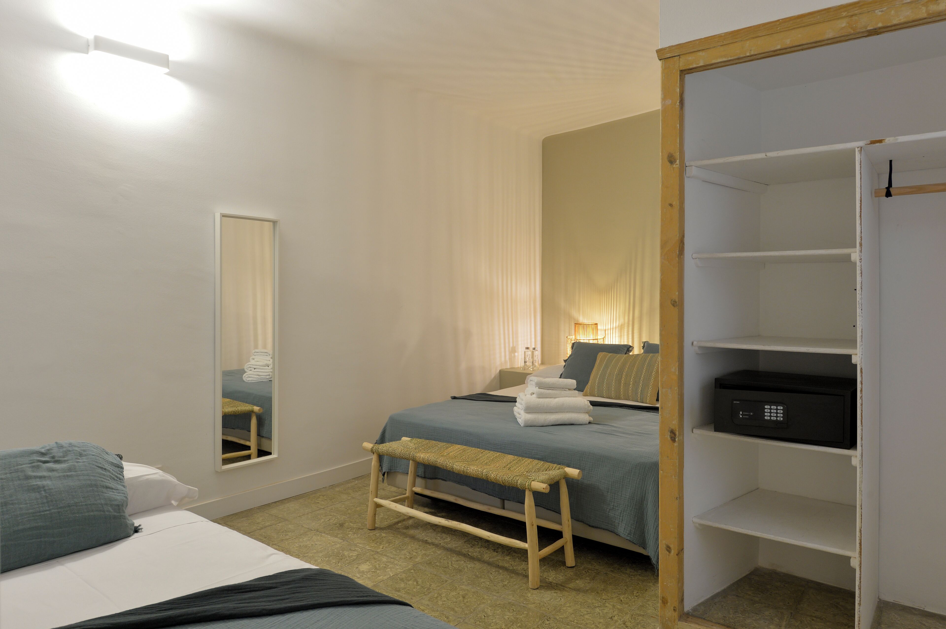 Un dormitorio con cama, banca, espejo, mesita de noche y armario.