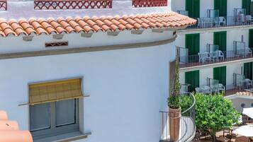 Een wit gebouw met terracotta dakpannen, groene luiken en een balkon met buitenmeubilair.