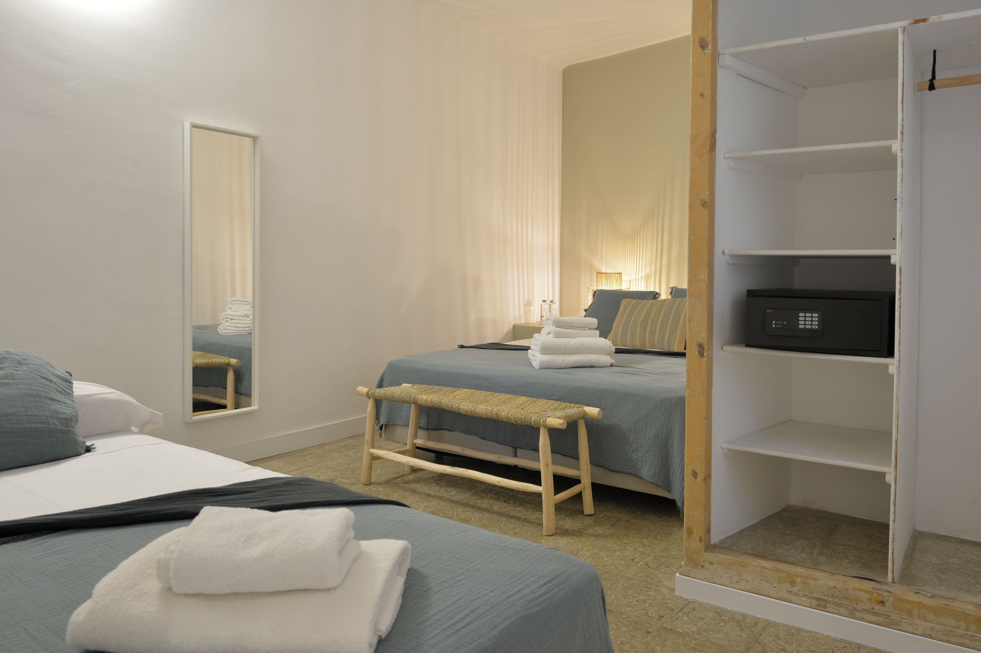 Een hotelkamer met twee bedden, een bankje, een kledingkast en een spiegel.
