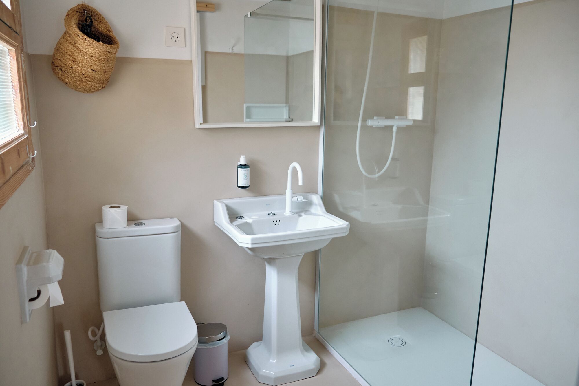 A modern bathroom with a toilet, pedestal sink, and glass-enclosed shower.