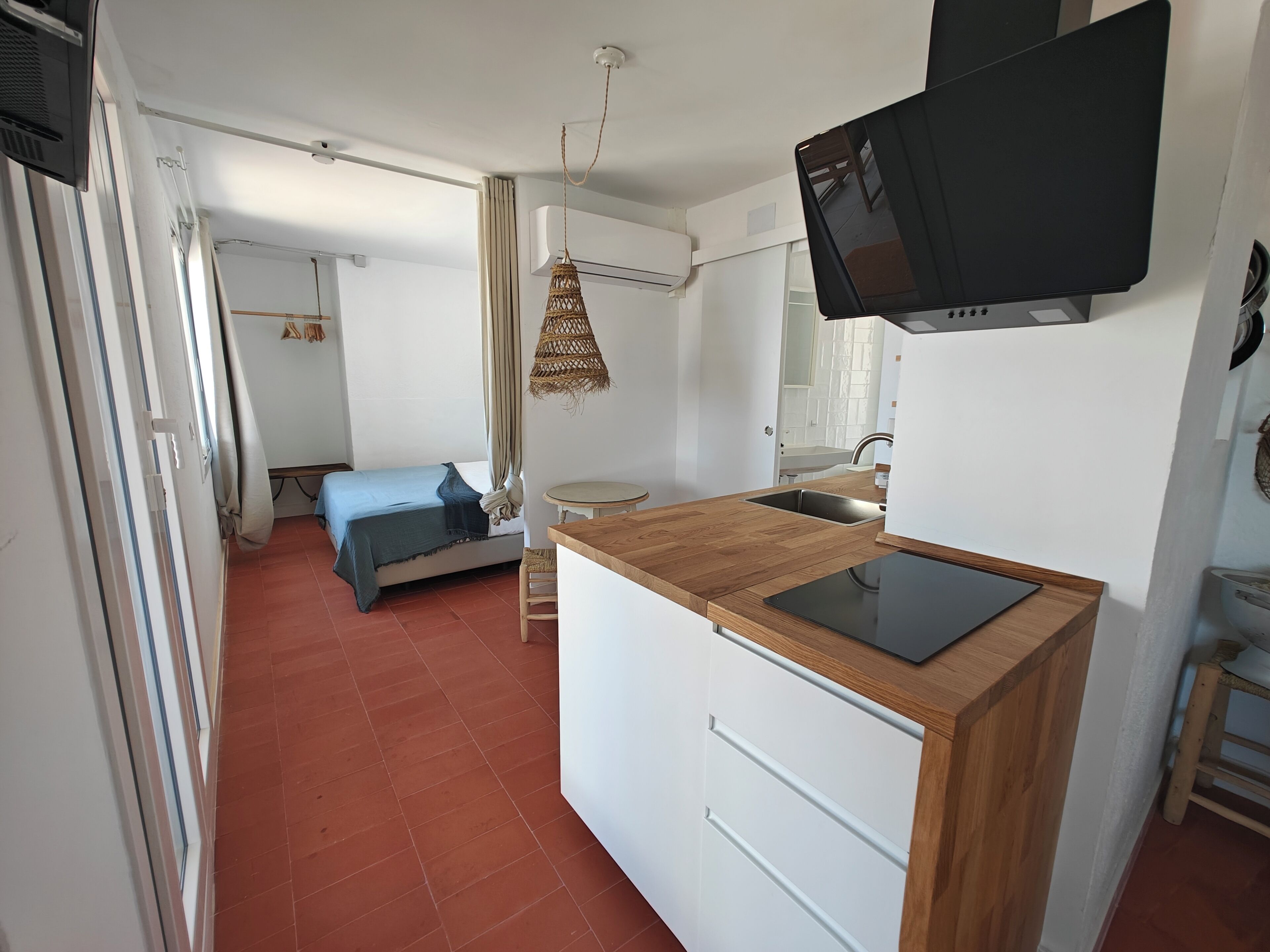 A compact room with a bed, a small kitchen area with a sink and a television, and a ceiling fan.