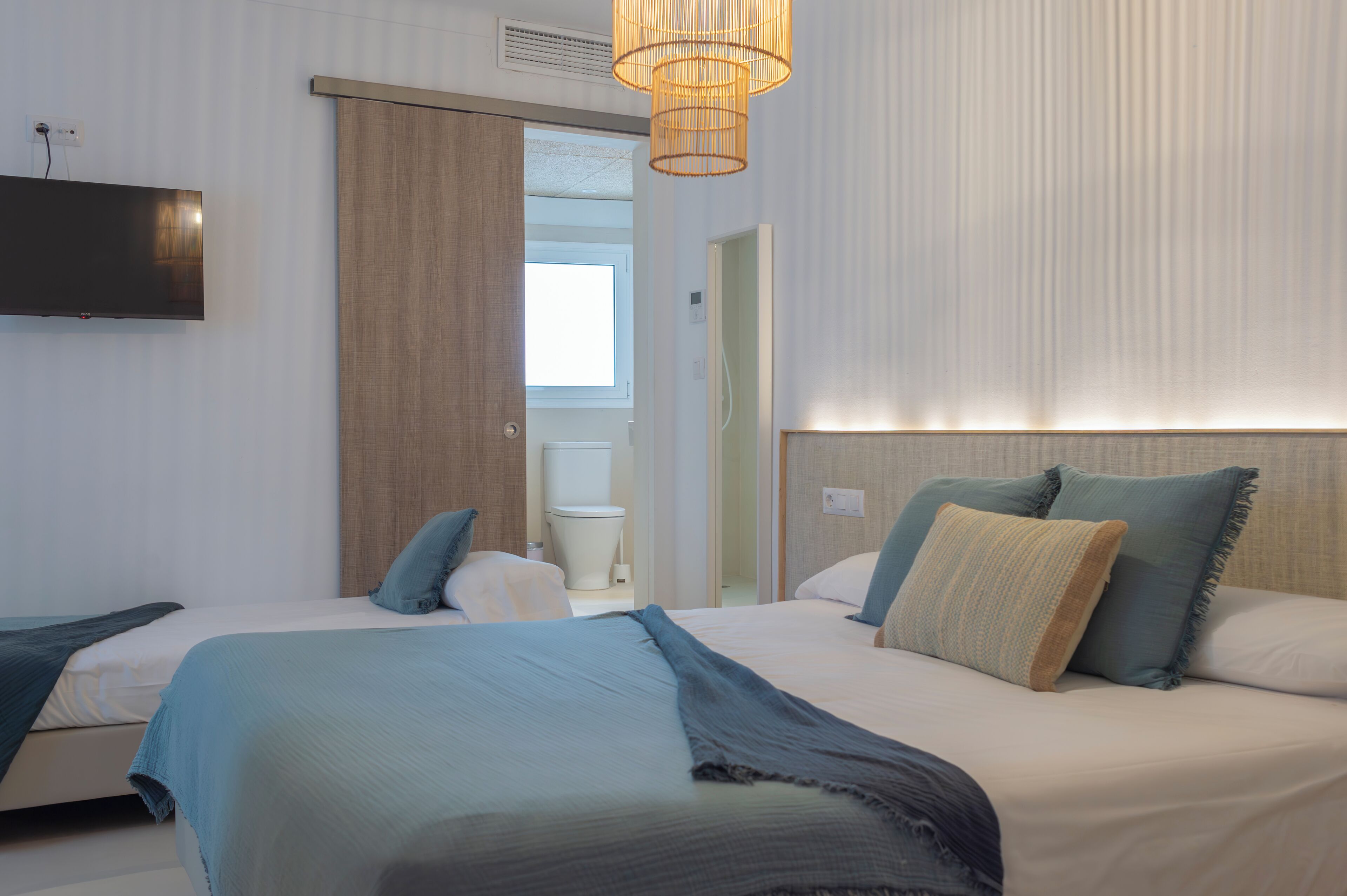 A hotel room with two beds, a television, a bathroom, and a large window.