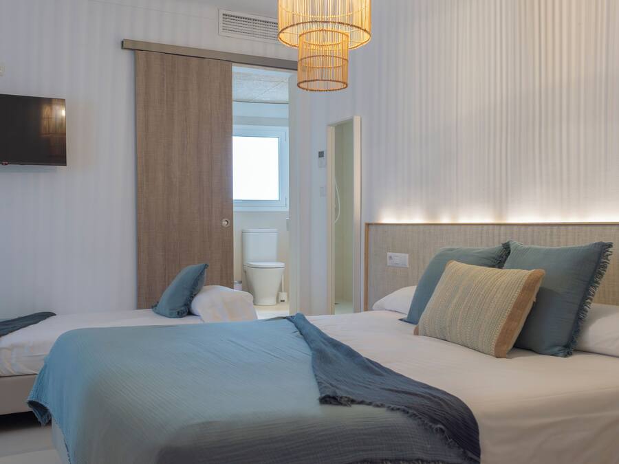 A hotel room with two beds, a television, a bathroom, and a large window.