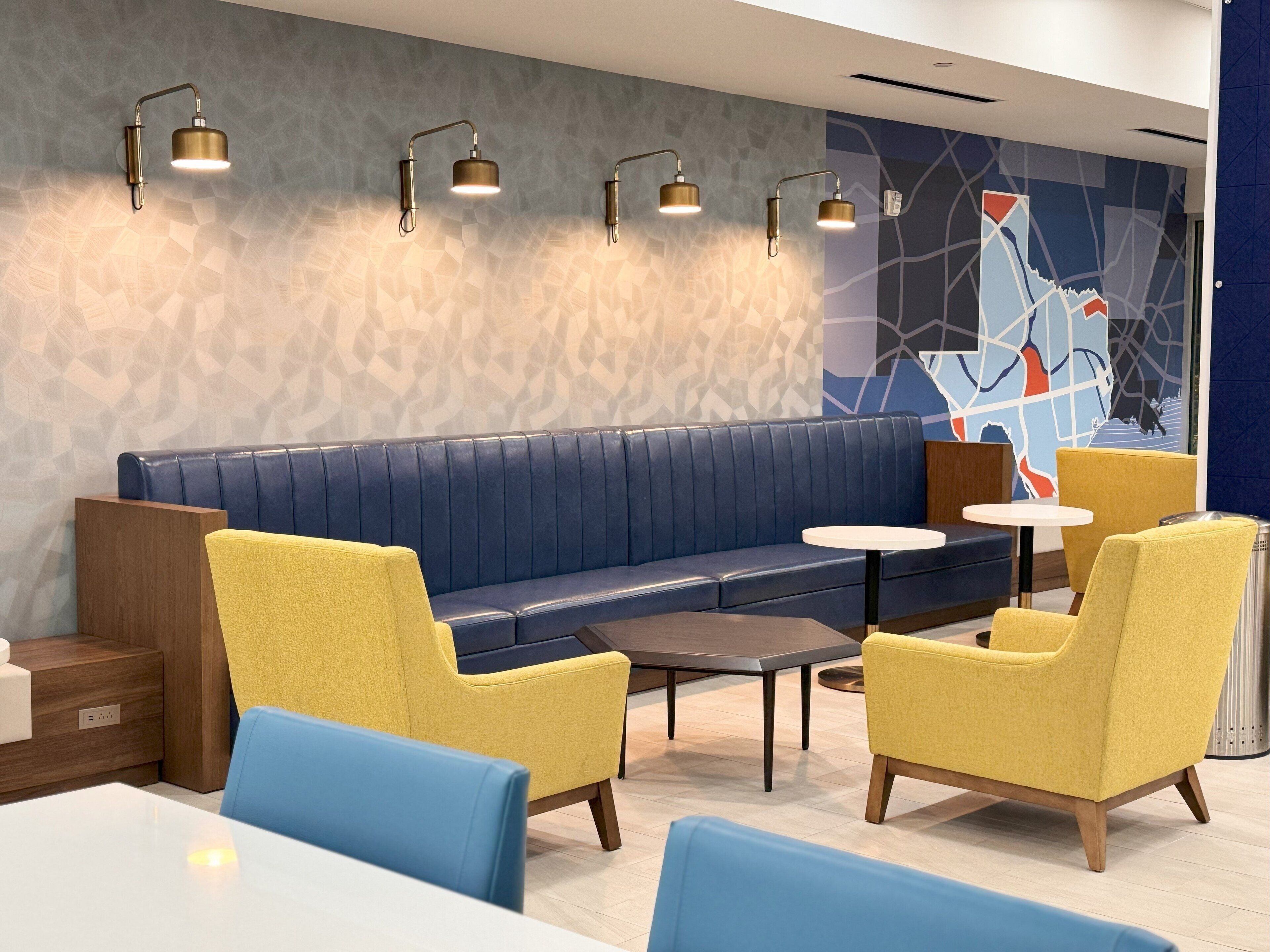 A modern lounge area with a blue sofa, yellow armchairs, and a small round table.