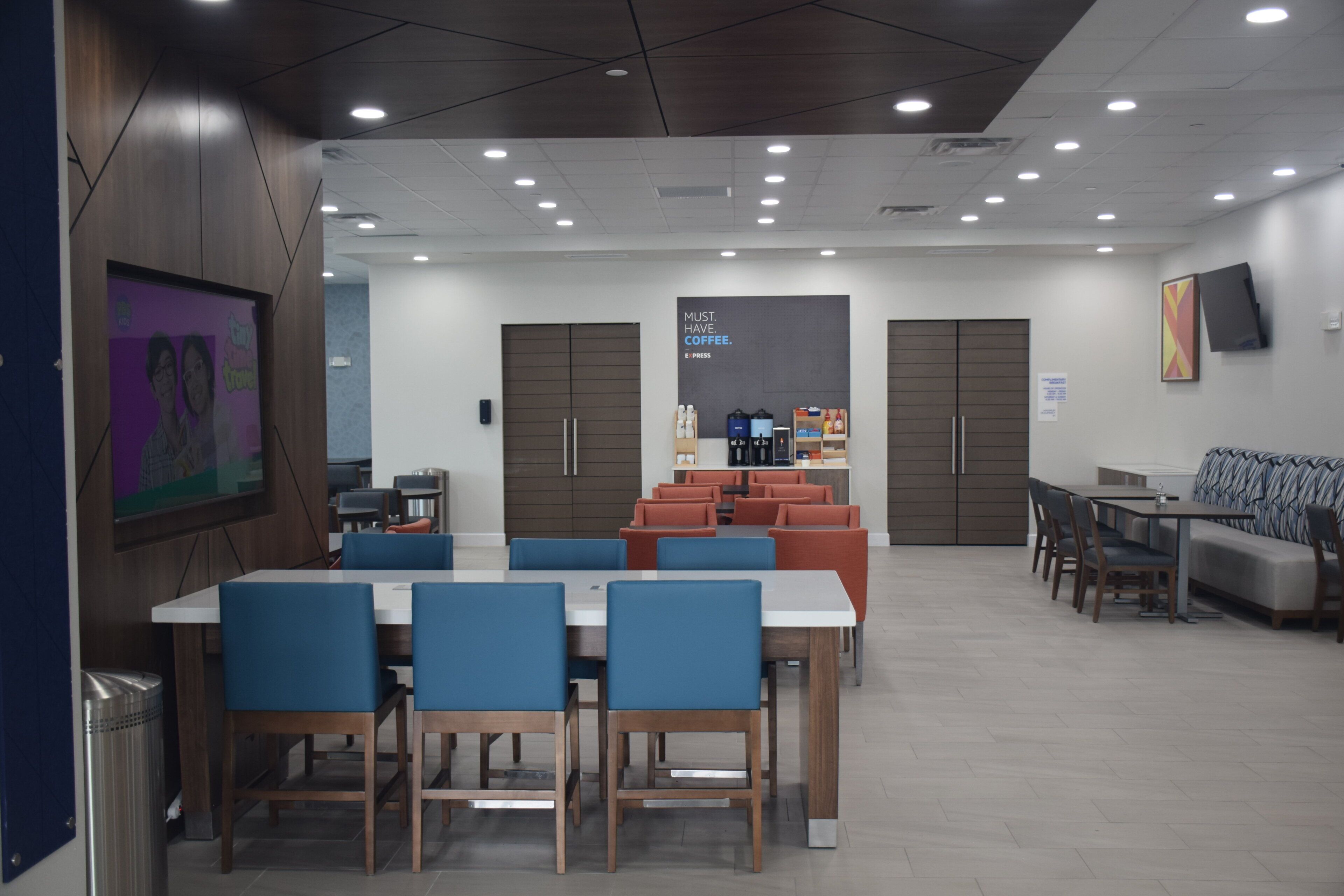 A modern dining area with tables and chairs, a coffee station, and a seating area with sofas and chairs.