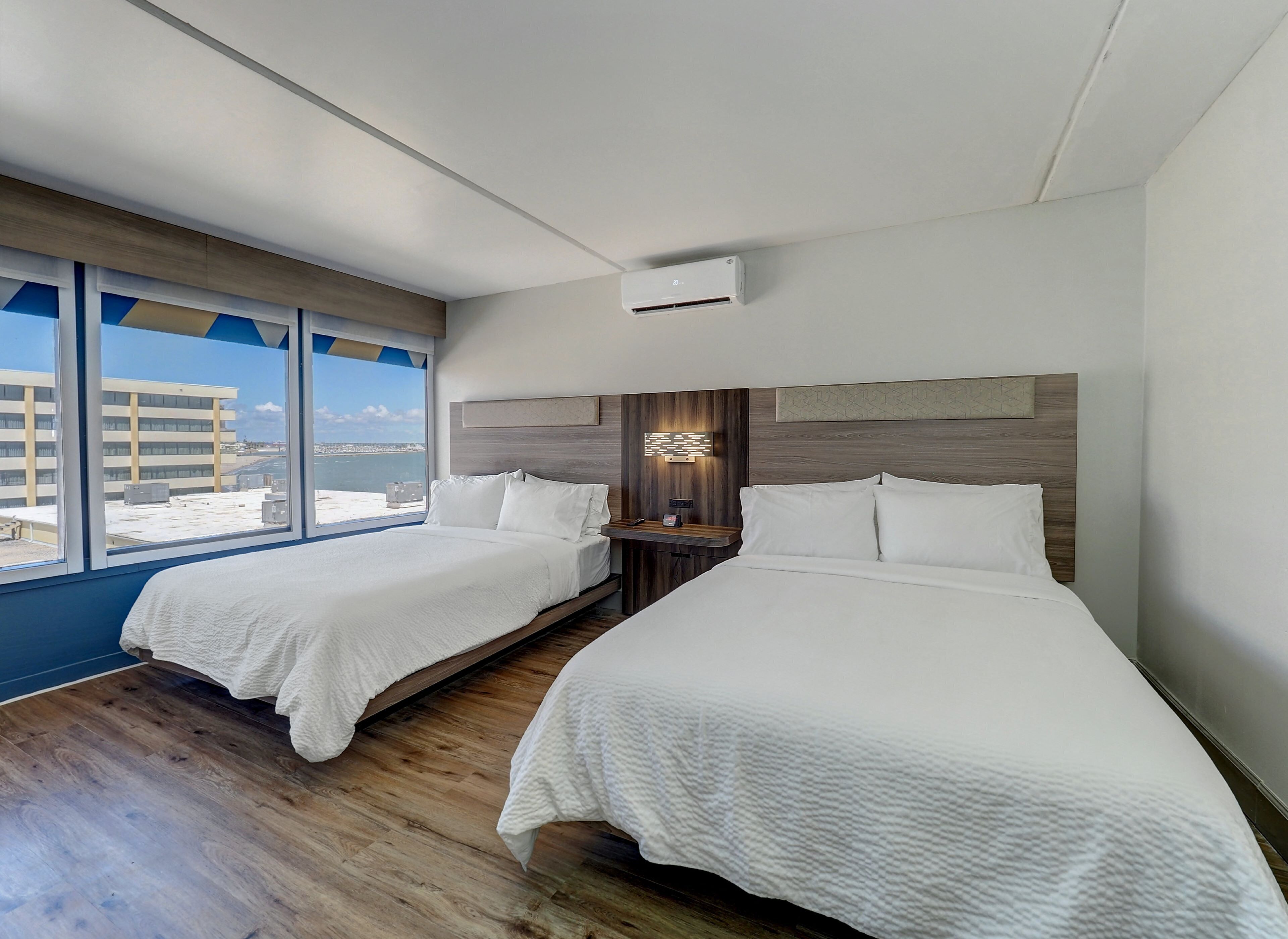 Camera d'albergo con due letti, una grande finestra vista edifici e un moderno lampadario.