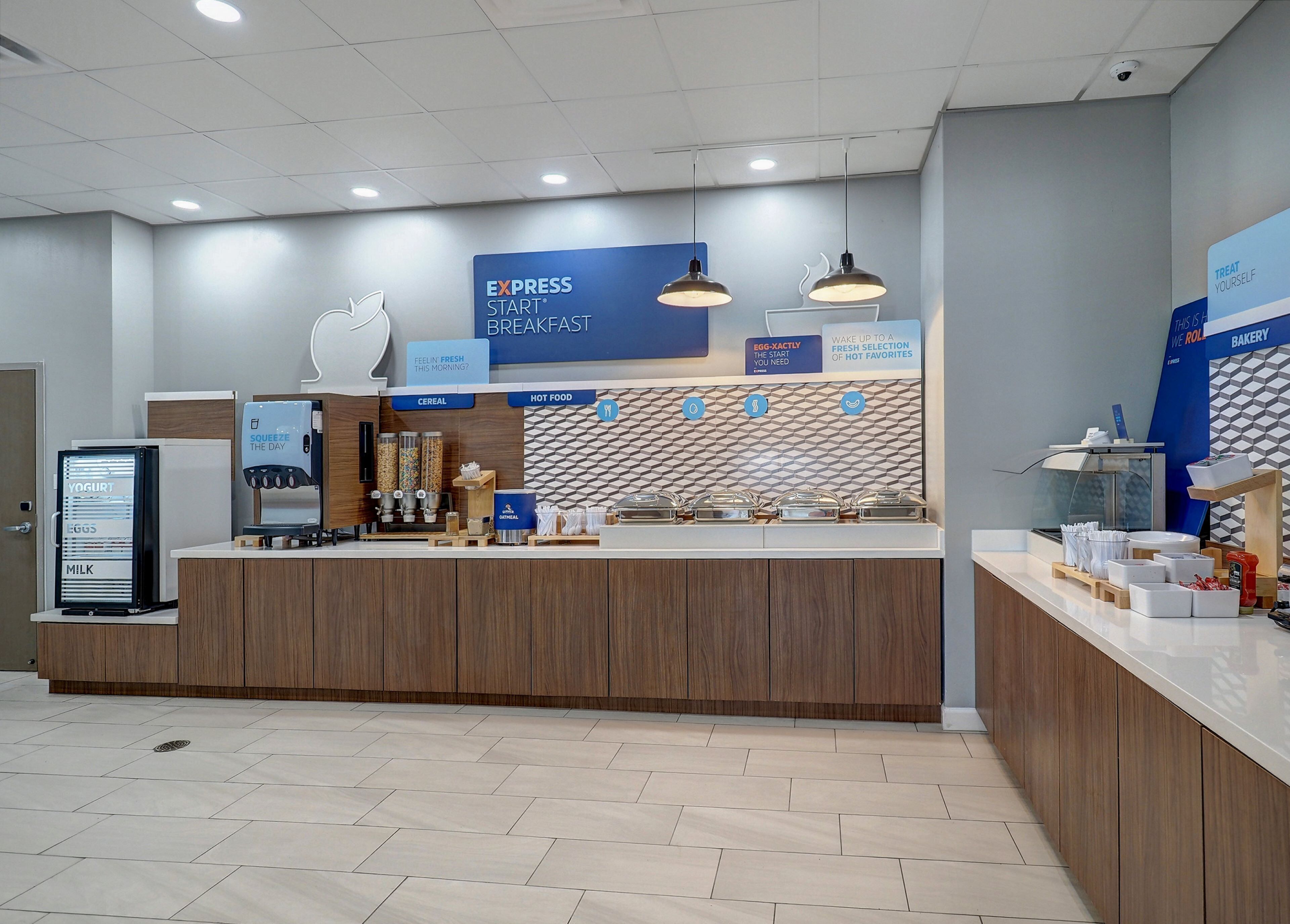 A breakfast area with a counter, yogurt and milk dispenser, cereal and hot food options, and a bakery section.